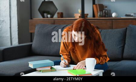 Student writing on notebook near cup at home Stock Photo