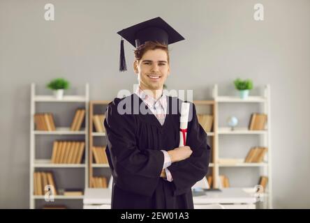 University graduate standing arms crossed, holding diploma and smiling at camera Stock Photo