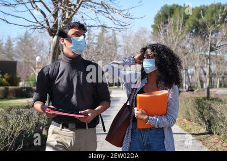 Two latin students wearing face mask and holding folders. New normal in the university campus. Stock Photo