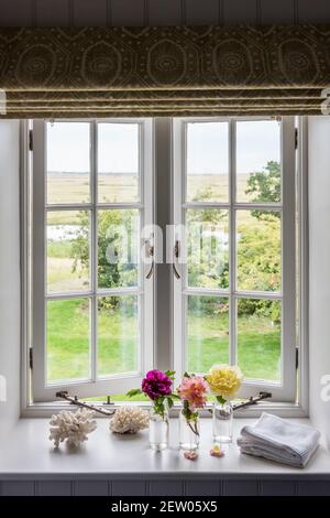Three single stem flowers in open window of off-grid farmhouse renovation. Stock Photo