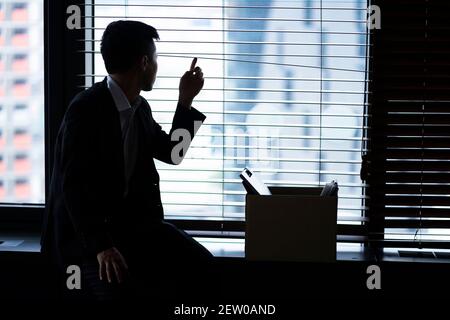 Fired businessman sitting with box of belongings by window Stock Photo