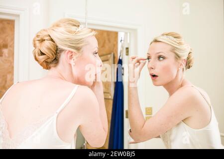 Bride applying mascara, looking at reflection in mirror Stock Photo