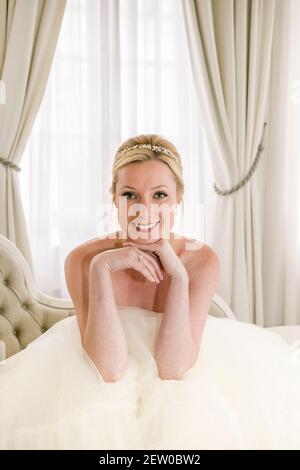Bride sitting down on chaise lounge within bridal suit Stock Photo