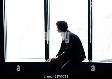 Businessman looking out of office window, looking pensive Stock Photo