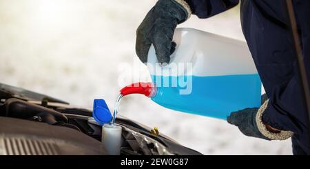 Man with gloves pouring antifreeze coolant into car reservoir in winter season. Stock Photo