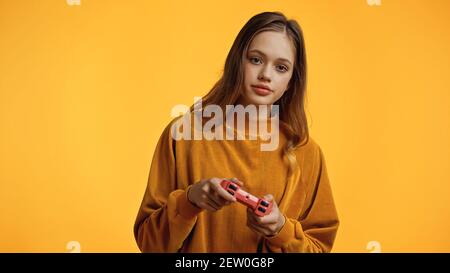 KYIV, UKRAINE - FEBRUARY 24, 2021: teenage girl playing video game isolated on yellow Stock Photo