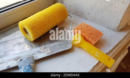 Slightly used yellow roller, putty knife and sponge on the windowsill Stock Photo