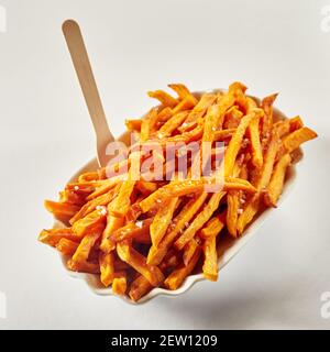 From above of yummy fried potato sticks with condiments and wooden fork in porcelain bowl on light background Stock Photo
