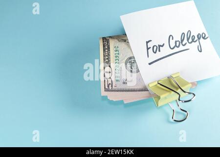 Text written note FOR COLLEGE with dollars cash money in clip, on copy space blue background - concept of financial planning to save money for purpose Stock Photo
