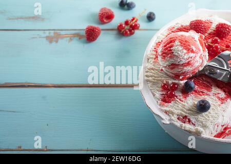 High angle of bowl of homemade frozen yogurt ice cream topped with red syrup and decorate with blueberries raspberries and red currants Stock Photo