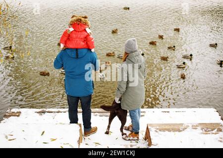 Full height back view unrecognizable portrait with one kid in winter sporty outfit walking outdoors near river with duck birds, weekend activities and Stock Photo