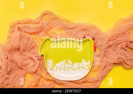 Easter frame background with green funny hen plate on hay over fabric and bright yellow color, flat lay Stock Photo