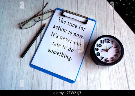 Motivational quote on blue clip board with alarm clock on wooden desk Stock Photo