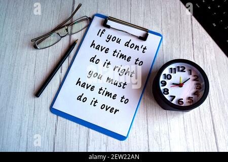 Motivational quote on blue clip board with alarm clock on wooden desk Stock Photo