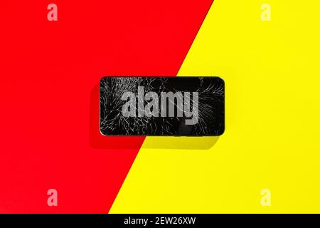 A black smartphone with a cracked display sits on a red and yellow background. Stock Photo