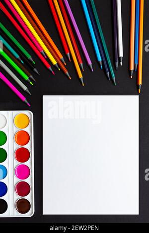 Blank sheet of paper, colored pencils and paints. Mock up, flat lay. Bright still life scene of stationery on a black background. Stock Photo