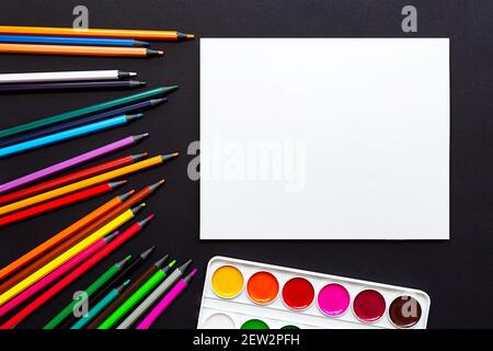 Blank sheet of paper, colored pencils and paints. Mock up, flat lay. Bright still life scene of stationery on a black background. Stock Photo