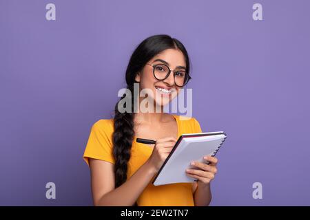 Indian woman holding pen writing in notebook at studio Stock Photo