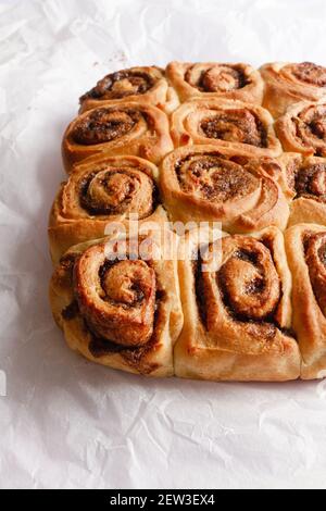 Freshly baked cinnamon rolls still attached together on a piece of white baking paper. Stock Photo