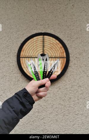 Throwing knives. Sport and hobby . Throwing knives in a man's hand and a target on the wall.Outdoor sports. Goal achievement concept. Stock Photo