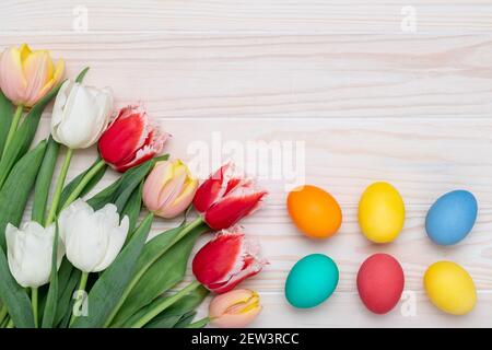 Happy Easter frame border, paschal eggs on a white wood background, bouquet of tulips, floral card, colorful festive template with copy space. Spring Stock Photo