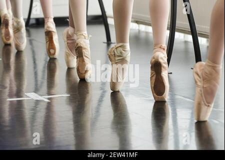 Tying her slippers before performance. Close-up of young ballerina in white tutu tying her slippers while sitting Stock Photo