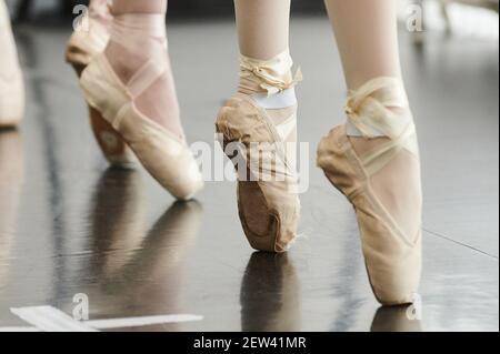 Tying her slippers before performance. Close-up of young ballerina in white tutu tying her slippers while sitting Stock Photo