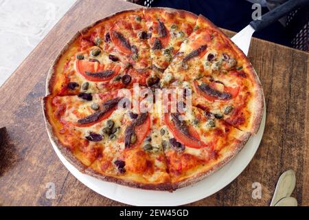 Anchovy and tomato pizza on a long handled pizza paddle in a Greek taverna on the Island of Kos Stock Photo