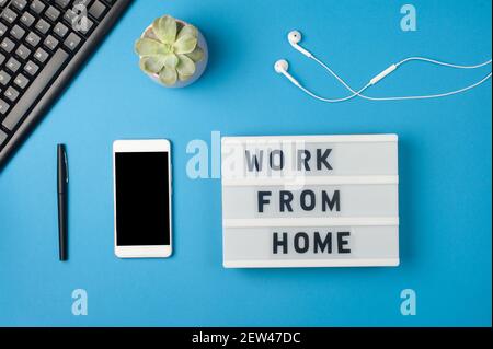 Work from home - text on display lightbox and smartphone mockup on blue background workplace. Black keyboard and white earphones. Freelance work conce Stock Photo