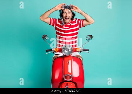 Portrait of handsome cheerful guy riding moped wearing diving mask having fun isolated over bright green turquoise color background Stock Photo