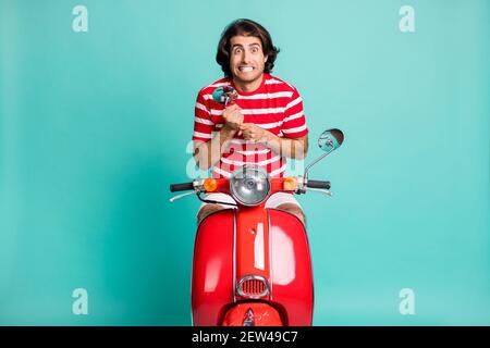 Portrait of handsome scared funky guy riding moped holding in hands mirror isolated over bright green turquoise color background Stock Photo