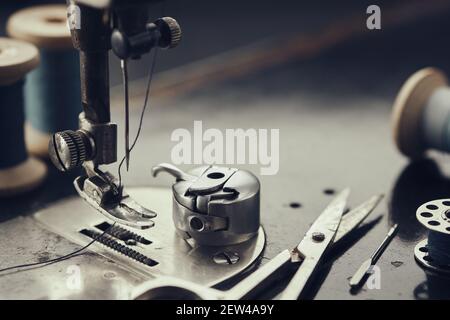 Close up on metal shuttle, foot of vintage sewing machine, scissors, spool of thread, sewing needles. Sewing items on working part of antique sewing m Stock Photo