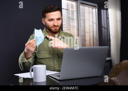 A man during a conference points at the camera with a medical mask pointing at it with his index finger. Calling for stringent safeguards against the Stock Photo