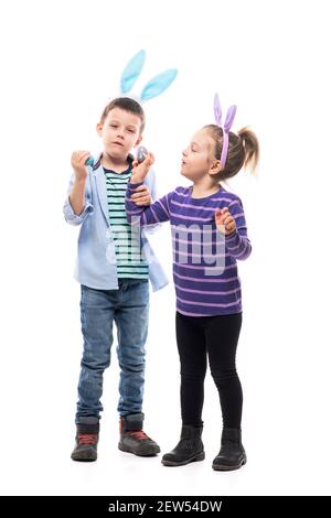 Happy little playful children siblings playing tapping eggs game with painted Easter eggs. Full body isolated on white background. Stock Photo