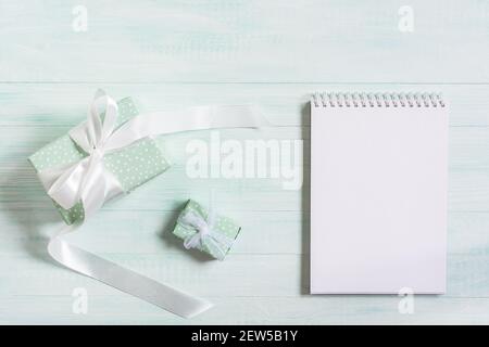 Gifts in a package with a white satin ribbon, a notebook on a wooden mint background. Top view, flat layout. The concept of a holiday, birthday, Mothe Stock Photo