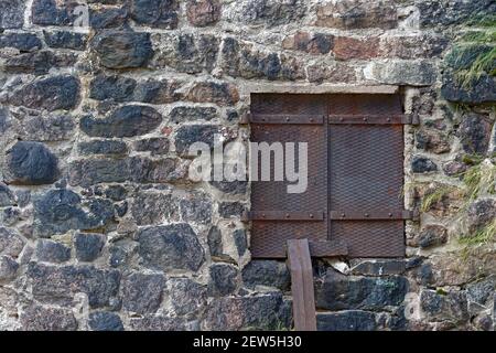 Rectangular window closed with reinforced iron sheet shutters on the stone wall of the old town hall. From the window of the world series. Stock Photo