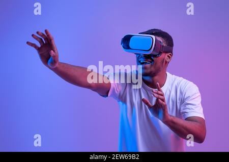 Amazed Black Man In VR Headset Experiencing Virtual Reality, Playing Video Game Stock Photo
