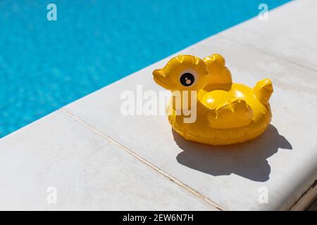 Inflatable yellow mini duck, cocktail stand near swimming pool on bright sunny day, copy space. Concept of summer vacation, entertainment, water, air, Stock Photo