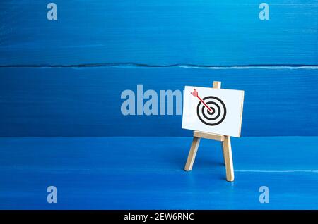 Easel with an arrow in target center. Direct hit, Bulls-eye, straight to the point. Marketing and targeting audience. Complete success. Advertising st Stock Photo