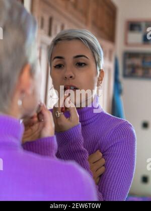Pretty girl putting on makeup in the mirror at home, confinement Stock Photo