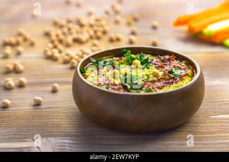 Homemade chickpea green hummus with herbs in round bamboo bowl, celery, carrot sticks on wood Stock Photo