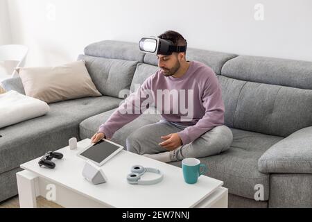 An adult man using a VR headset and a tablet while sitting on a sofa Stock Photo