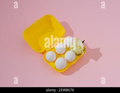 2021 Easter minimal creative concept. Five white eggs and a white rose in a bright yellow box on a pastel pink background.Still life retro composition Stock Photo