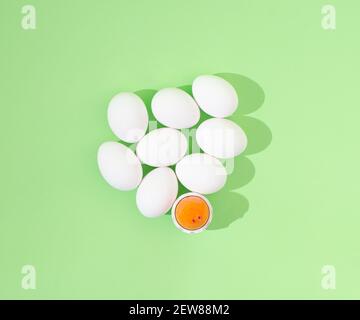 2021Easter, minimal creative concept. White whole eggs and a broken one with yolk, on pastel green background. Creative flat lay. Still life. Stock Photo