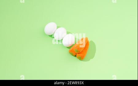 2021 Easter minimal composition. Three white eggs and three carrots on a pastel green background. Minimal creative flat lay composition. Stock Photo