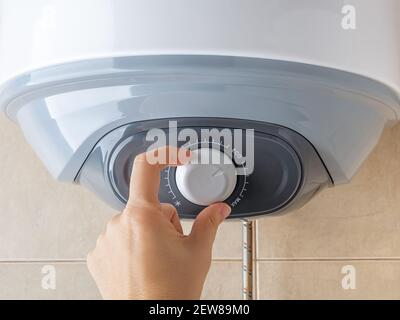 Woman hand rotates water heater temperature adjuster to the Eco position for economical use of electricity. Modern home appliances with energy saving Stock Photo