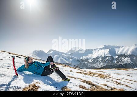 The blonde hiker lies in the snow and enjoys the beautiful mountain views. Stock Photo