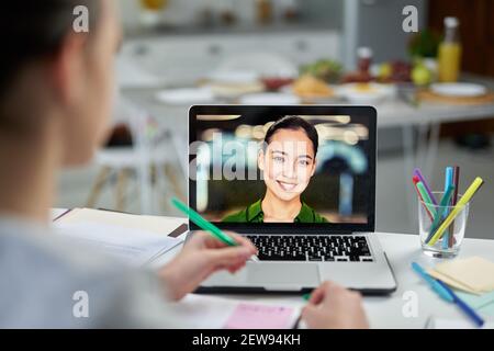 Attractive young female teacher smiling to her students, using video chat app during online lesson. Home schooling during quarantine. Focus on laptop screen Stock Photo
