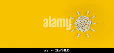 Sun shape made from white pills capsules on yellow backdrop with copy space. Stock Photo