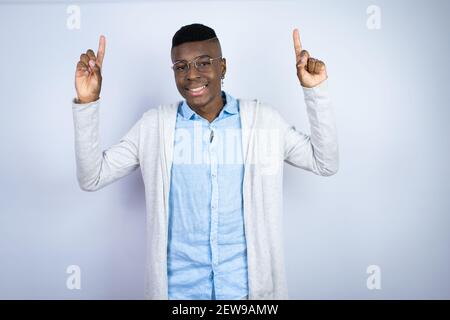 Young handsome african american man wearing casual clothes smiling, looking at the camera and pointing up with fingers and raised arms Stock Photo